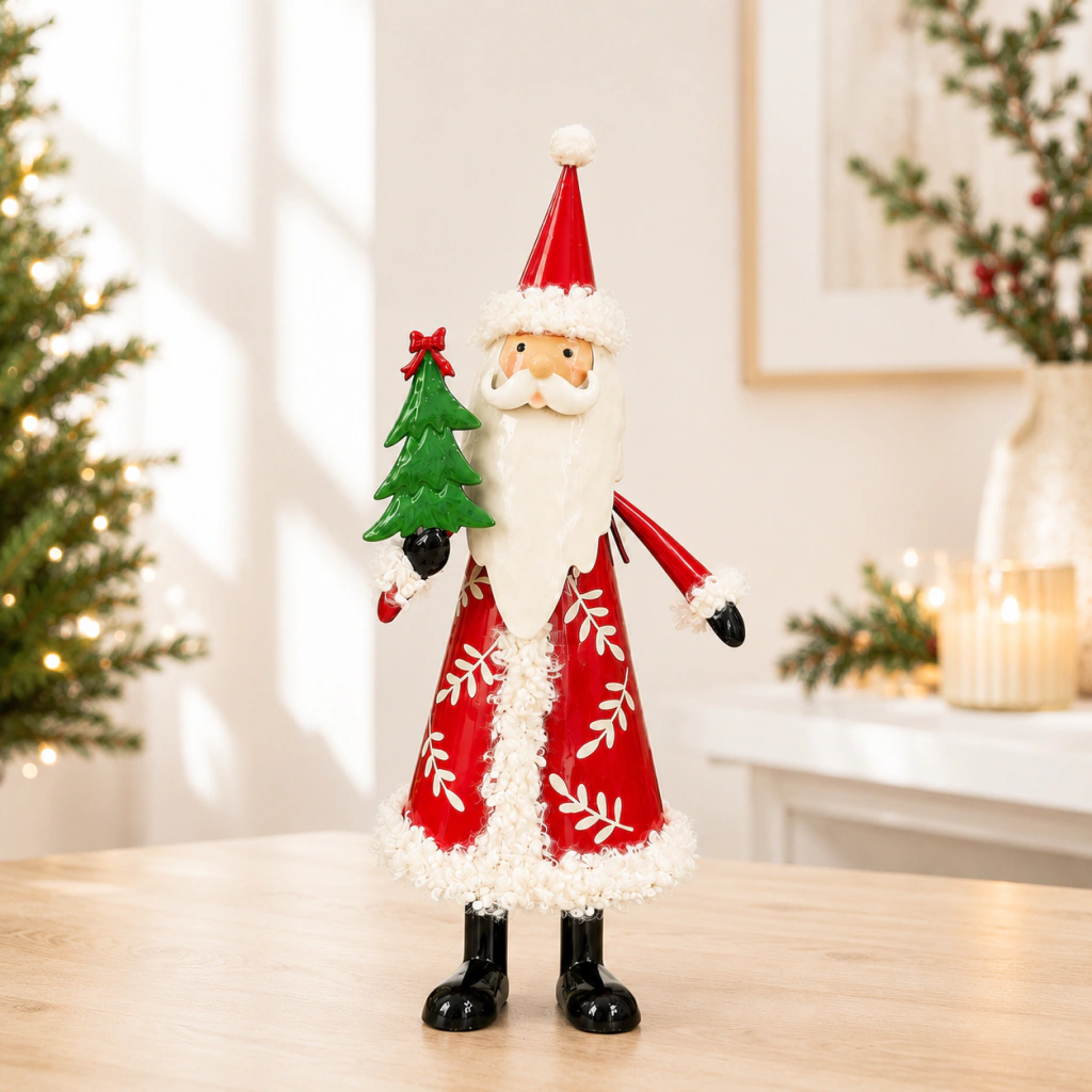 Figura decorativa de Santa Claus de metal rojo sosteniendo un árbol de Navidad verde, con detalles blancos y negro en las botas y guantes, sobre una mesa de madera en un ambiente navideño.