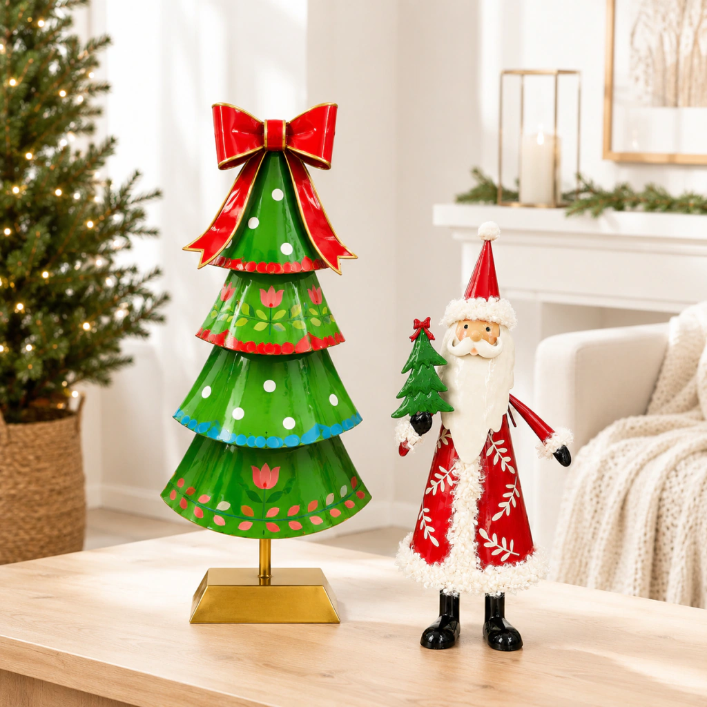 Adorno navideño de Santa Claus en metal rojo con detalles blancos sosteniendo un árbol de Navidad junto a un árbol navideño verde decorado con lazo rojo y base dorada sobre mesa de madera